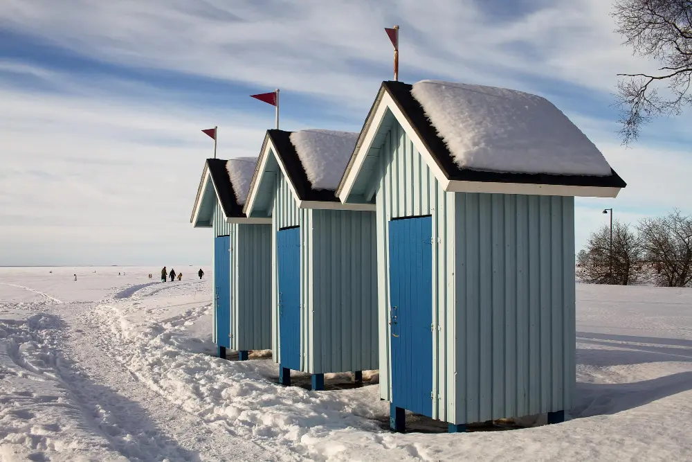 Trending European destinations showing colorful seaside cabins along Oulu’s frozen coastline in winter.