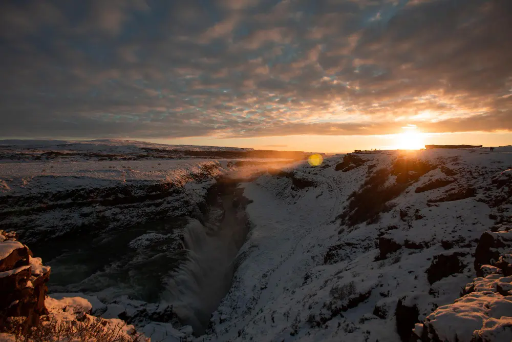 A wide-angle landscape shot of a hiker on a vibrant green cliff overlooking a black sand beach and ocean under a bright sun, symbolizing a summer trip and how to plan a trip to Iceland.