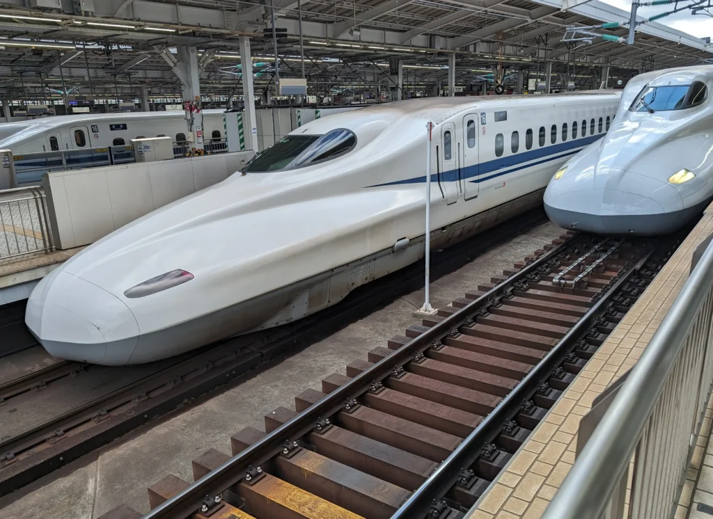 A high-speed Shinkansen bullet train at a station platform, illustrating transportation costs and how much is to travel to japan.